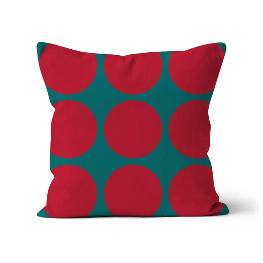Square shaped cushion with large red spotty pattern on plain dark teal green background.