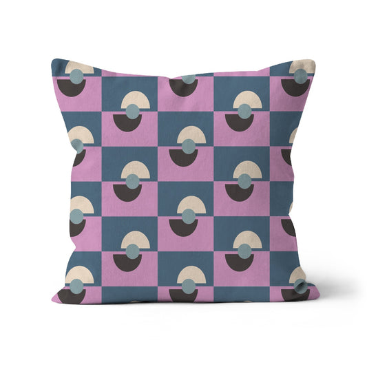 Square-shaped cushion covered with a graphic repeat pattern of lilac and blue/grey oblong shapes with black and beige half moon graphic shapes